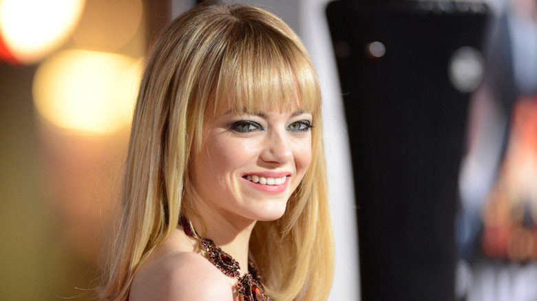 Emma Stone wearing blonde hair with blunt bangs and a chunky jeweled necklace