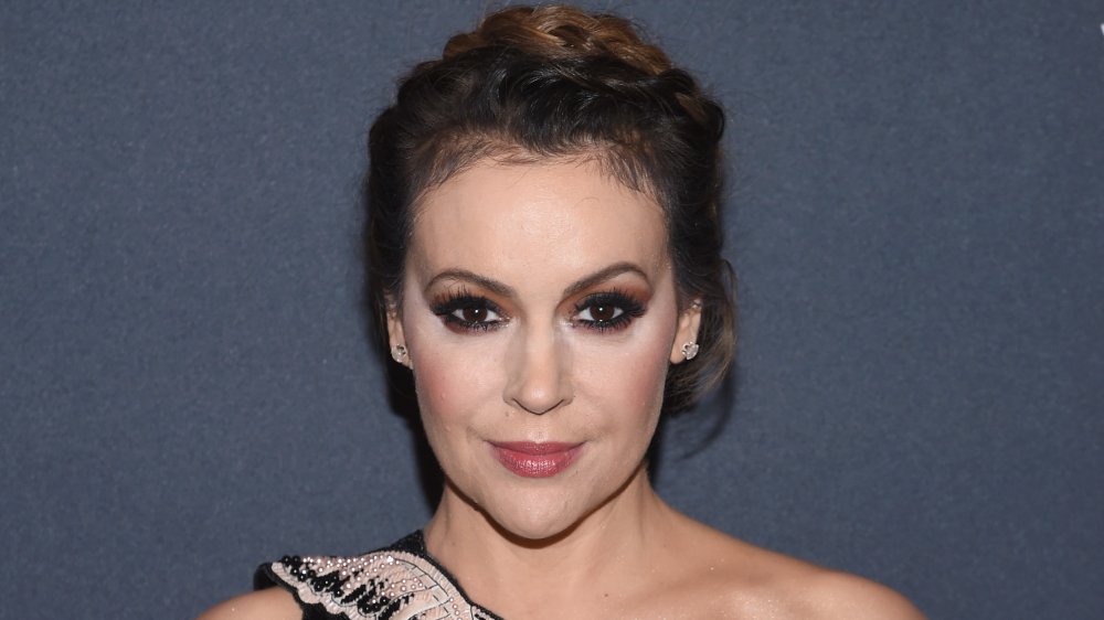 Alyssa Milano in a braided up-do and bejeweled dress, with a small smile and striking a power pose on the red carpet