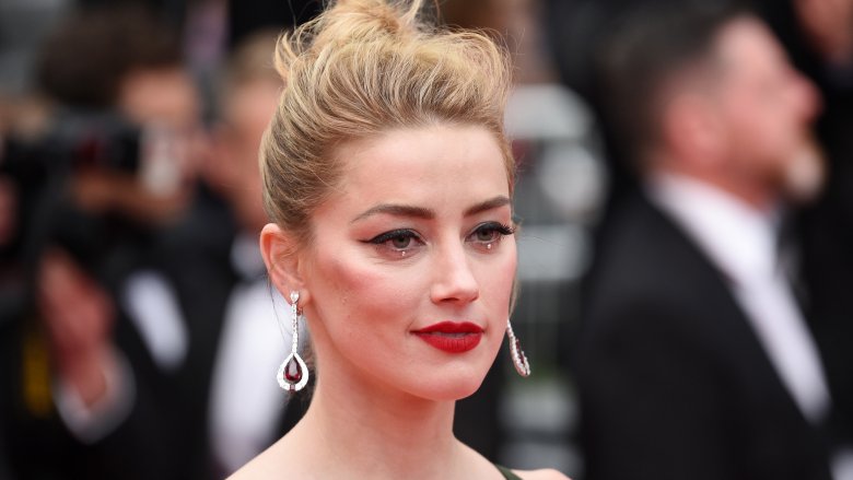 Amber Heard smirking at an event, with her hair in an up-do and wearing under-eye jewels