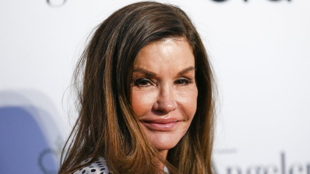 Janice Dickinson smirking on the red carpet, wearing a white outfit with black polka dots