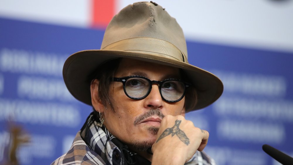 Johnny Depp wearing a brown hat, tinted glasses, plaid shirt, and bandanna scarf, looking serious