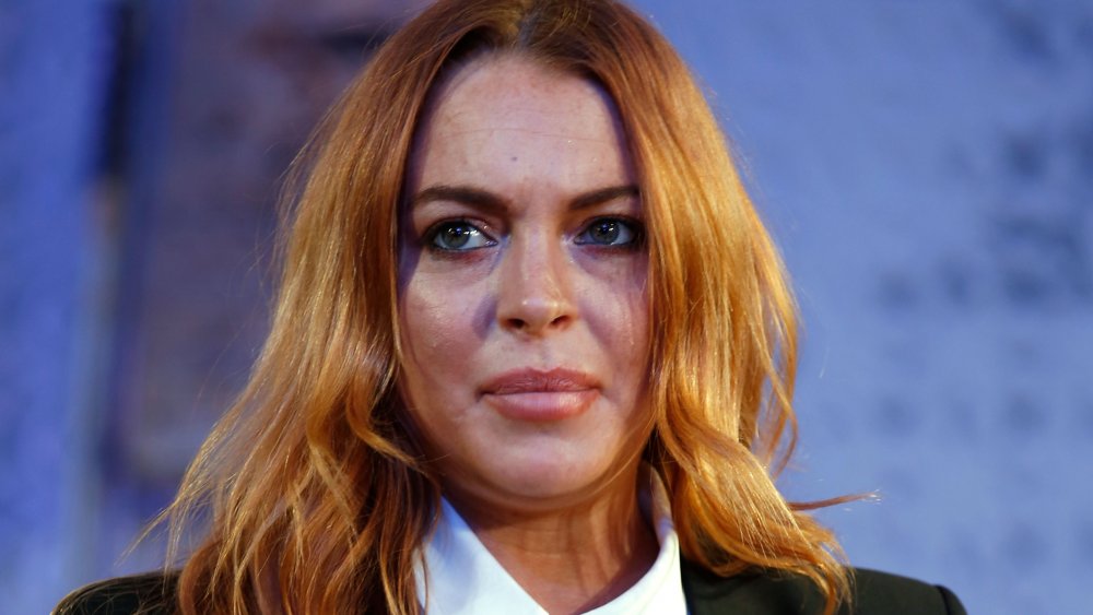 Lindsay Lohan wearing a black blazer and white shirt in a play, with a serious expression