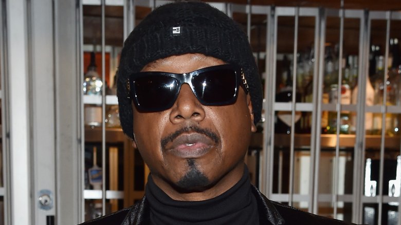 MC Hammer wearing all black beanie, sunglasses, turtleneck, and jacket, posing with a serious expression