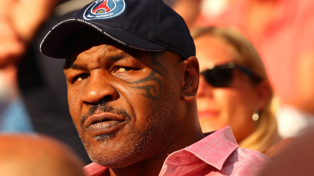 Mike Tyson wearing a pink button-down shirt and a blue baseball cap, frowning