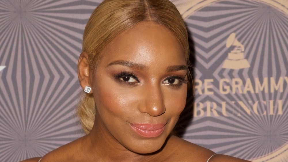 NeNe Leakes in a white, lacy, thin-strapped dress, smirking while posing at an event