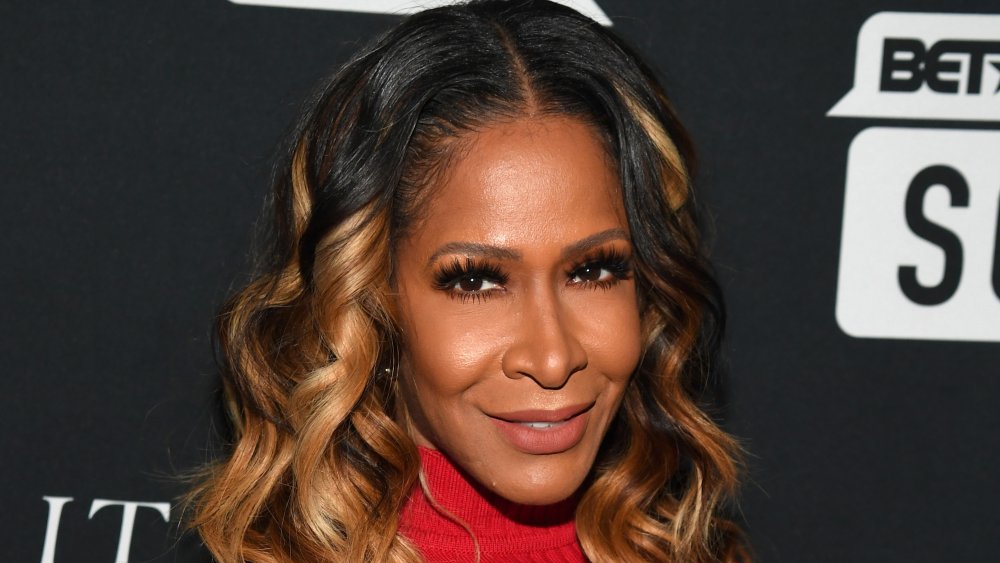 Sheree Whitfield in a red turtleneck sweater dress, smiling on the red carpet