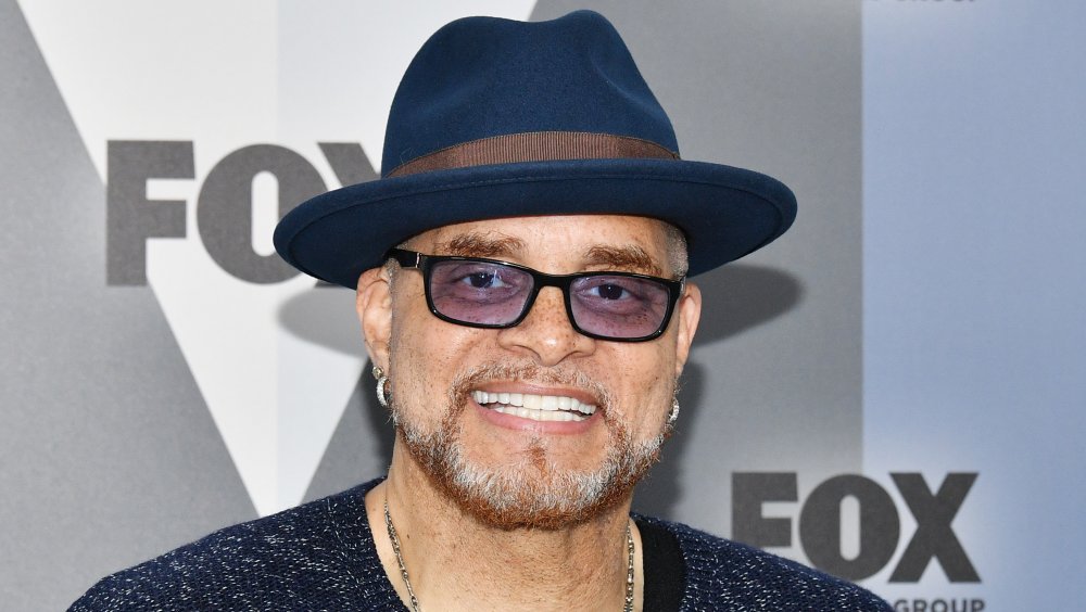 Sinbad wearing a blue hat, tinted glasses, and earrings, smiling at an event