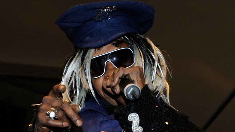 Sly Stone wearing a black-and-blue outfit with matching hat and sunglasses, performing live