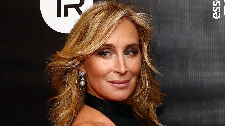 Sonja Morgan wearing a black dress and pearl earrings, smirking over her shoulder on the red carpet