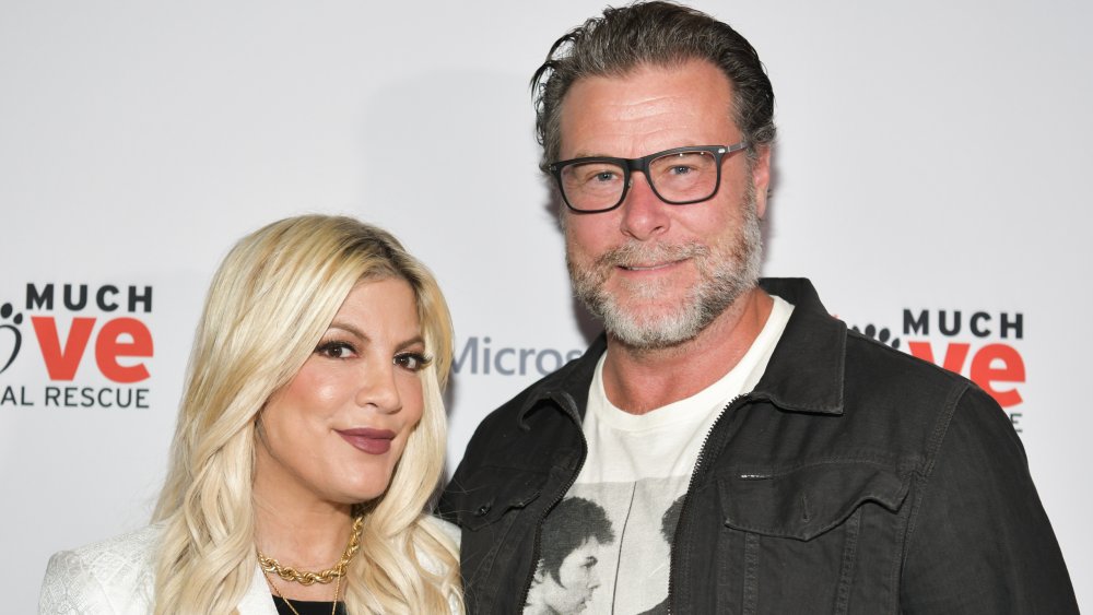 Tori Spelling in a white blazer and Dean McDermott in a black jacket, both with small smiles and posing next to one another at an event