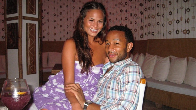 Chrissy Teigen sitting on John Legend's lap smiling