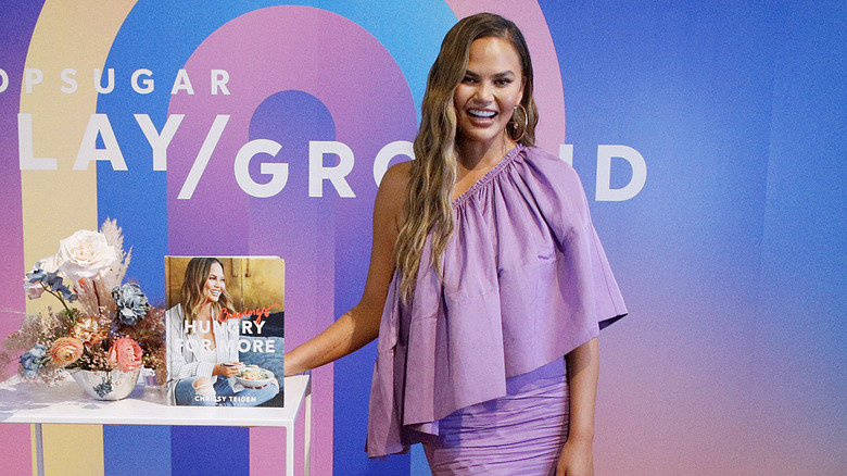 Chrissy Teigen poses with her cookbook