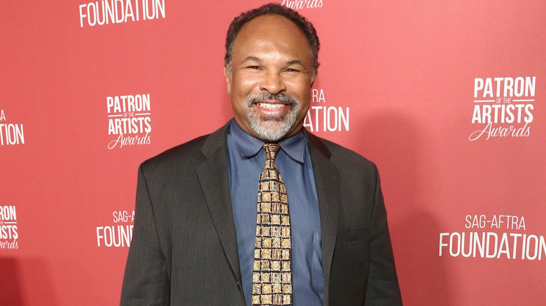 Geoffrey Owens on the red carpet in gold patterned tie, blue shirt, and dark gray blazer