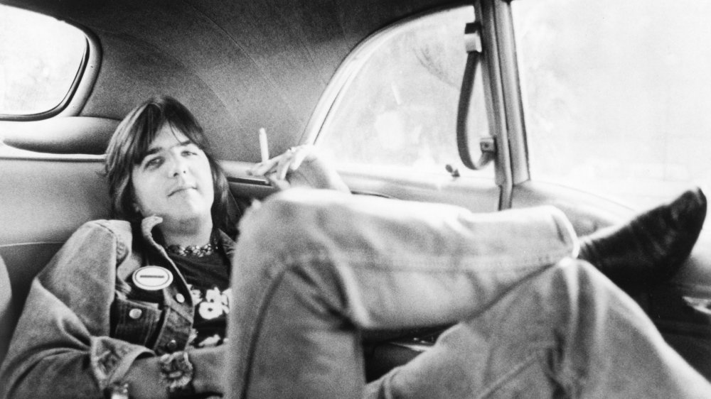 Gram Parsons reclining in a car, smoking a cigarette