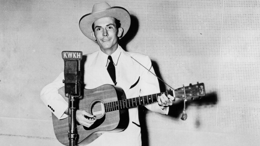 Hank Williams with his guitar, posing in front of microphone