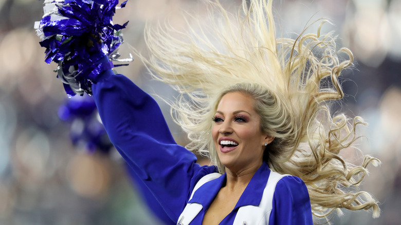 Dallas Cowboy Cheerleader, waving pom pom on field in 2019