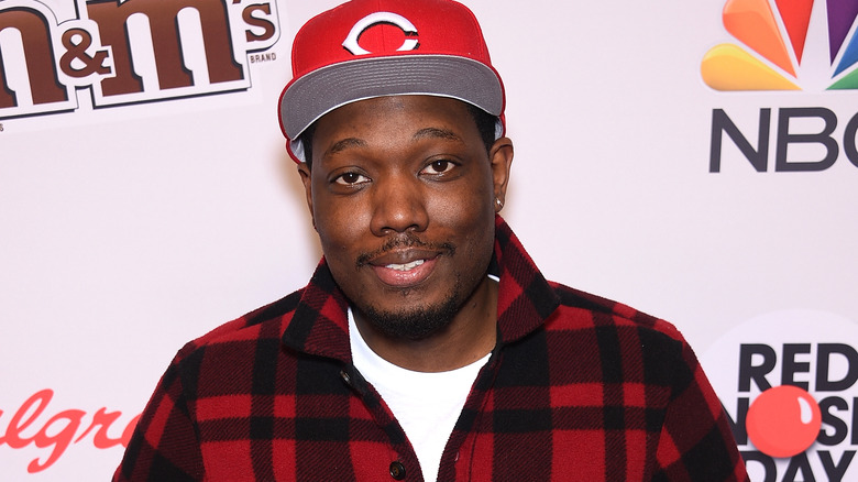 Michael Che posing in red cap