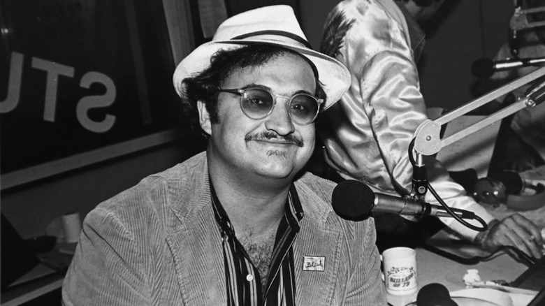 John Belushi smiling wearing a hat and sunglasses