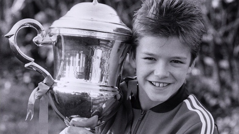 Young David Beckham smiling with a trophy