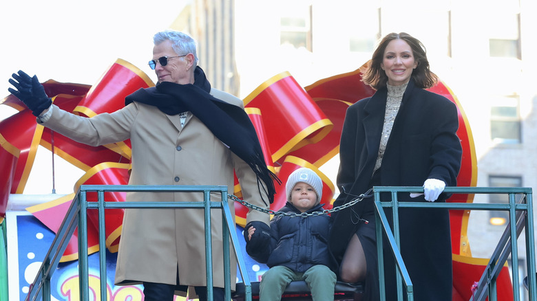 David Foster and Katharine McPhee stand on a Thanksgiving parade float with their toddler