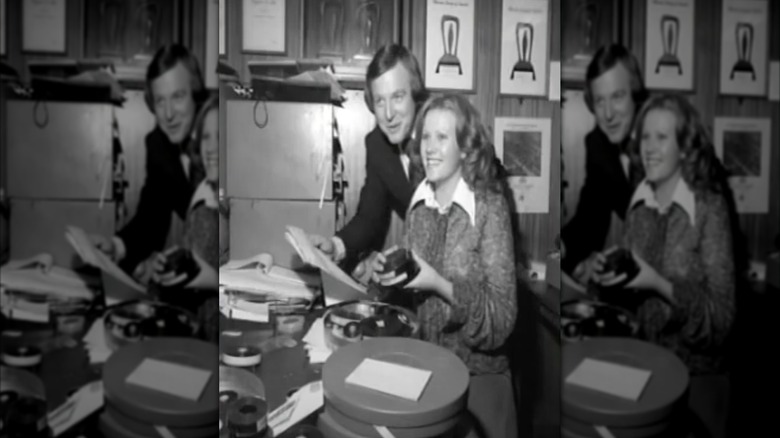 Deborra-Lee Furness smiling and sitting at a desk with John Sorell standing behind her