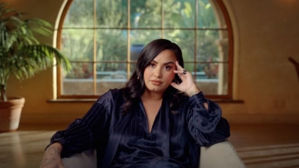 Demi Lovato sitting on a couch in front of a window