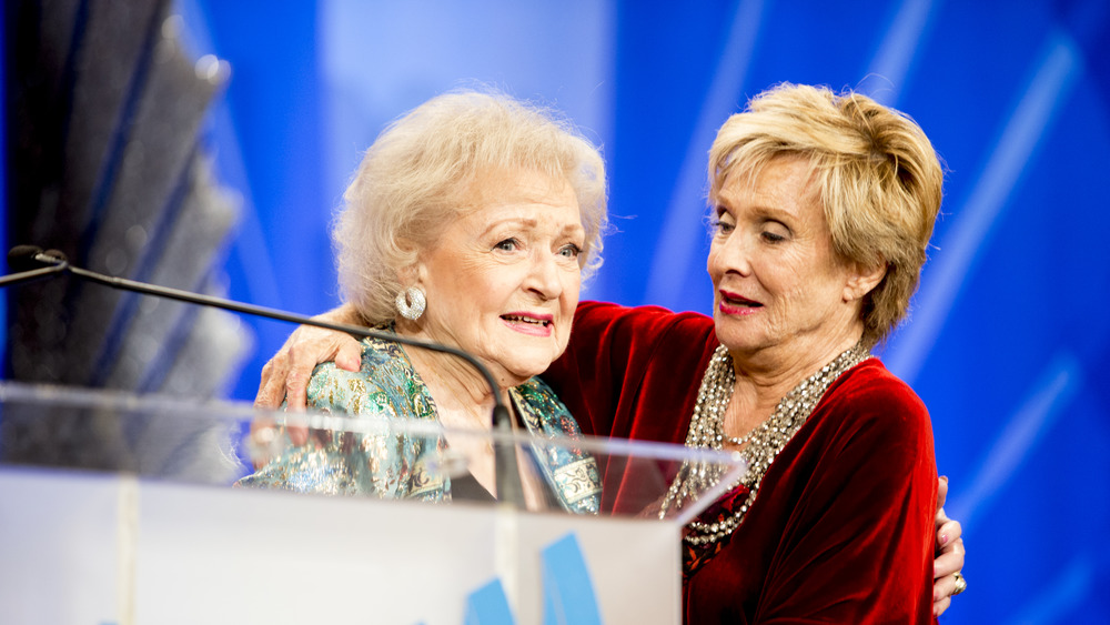 Betty White wearing silver earrings leans in for a hug from Cloris Leachman at an event