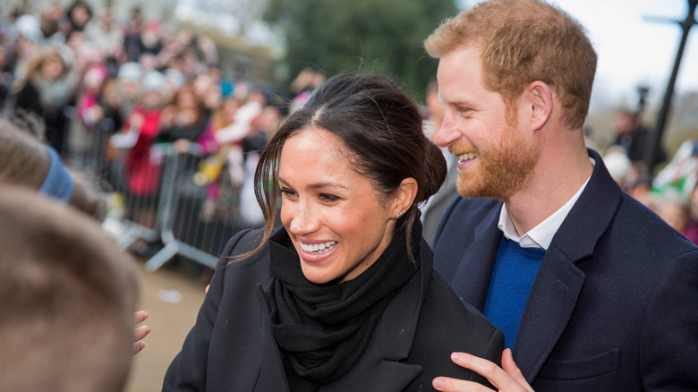 Prince Harry laughing behind Meghan Markle