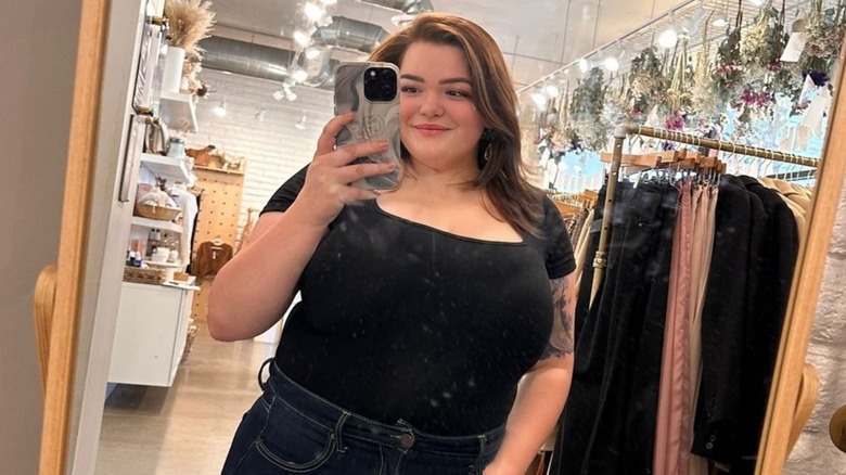 Bonnie Chapman smiling and taking mirror selfie inside clothing store