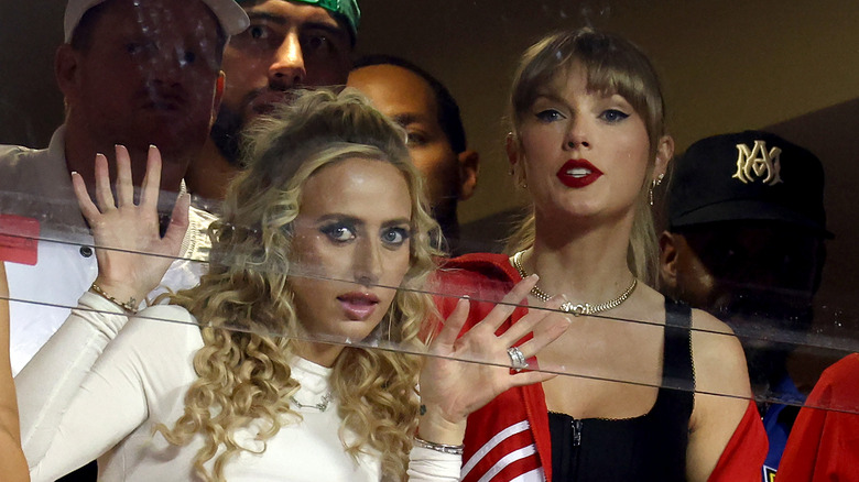 Brittany Mahomes with hands on glass beside Taylor Swift