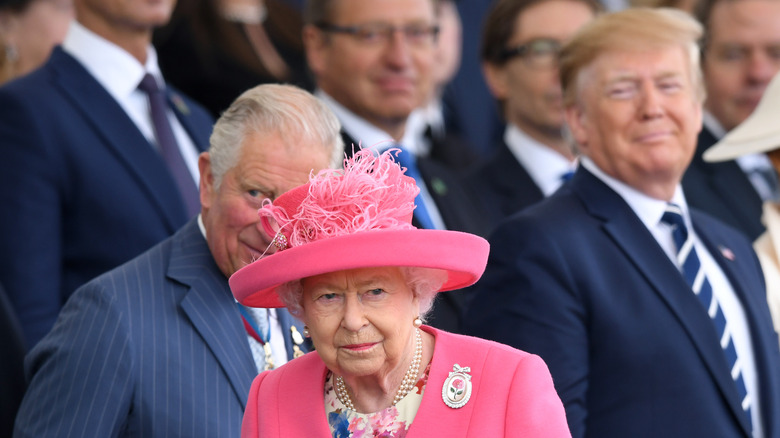 Donald Trump smiling at Queen Elizabeth as she walks away.