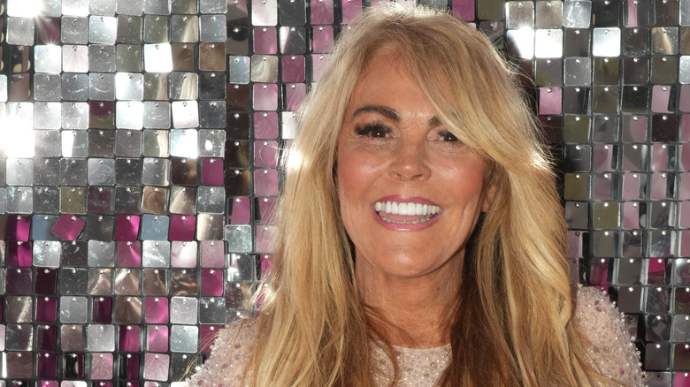 Dina Lohan posing at a party in front of wall of reflective decroations