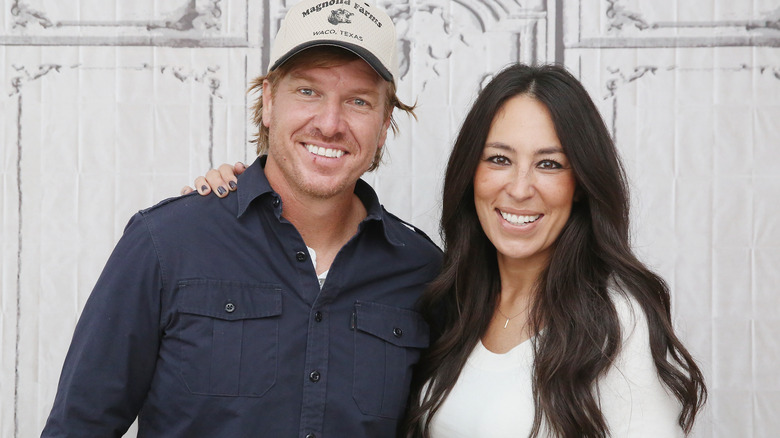 Chip Gaines wearing Magnolia Farms hat; Joanna Gaines wearing a white sweater and putting her arm around him