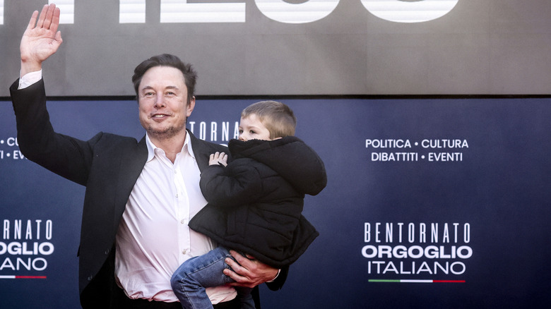 Elon Musk waving and holding his son