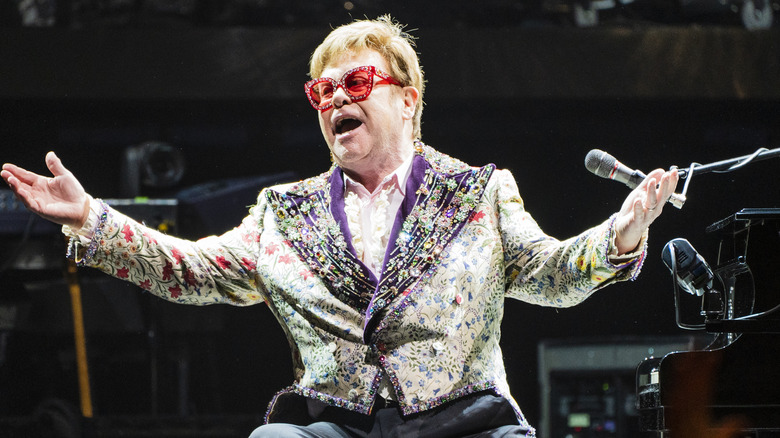 Elton John sings on stage in front of a piano