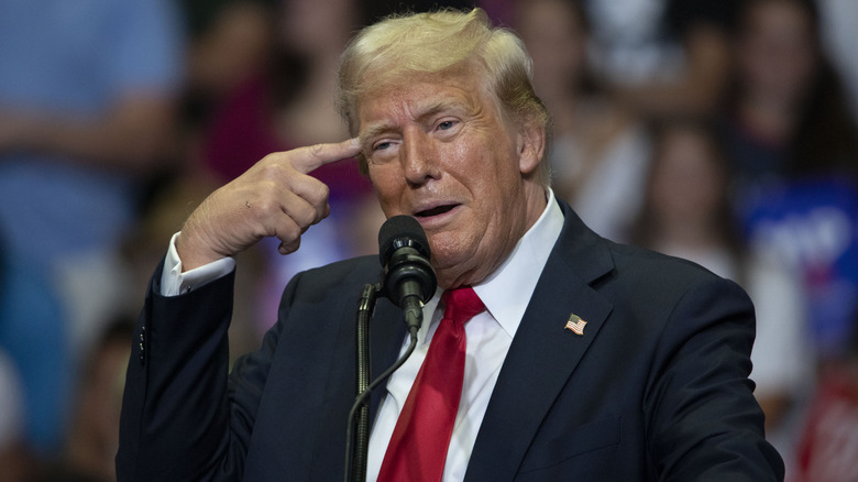 Donald Trump pointing at his head while addressing a crowd in Grand Rapids.