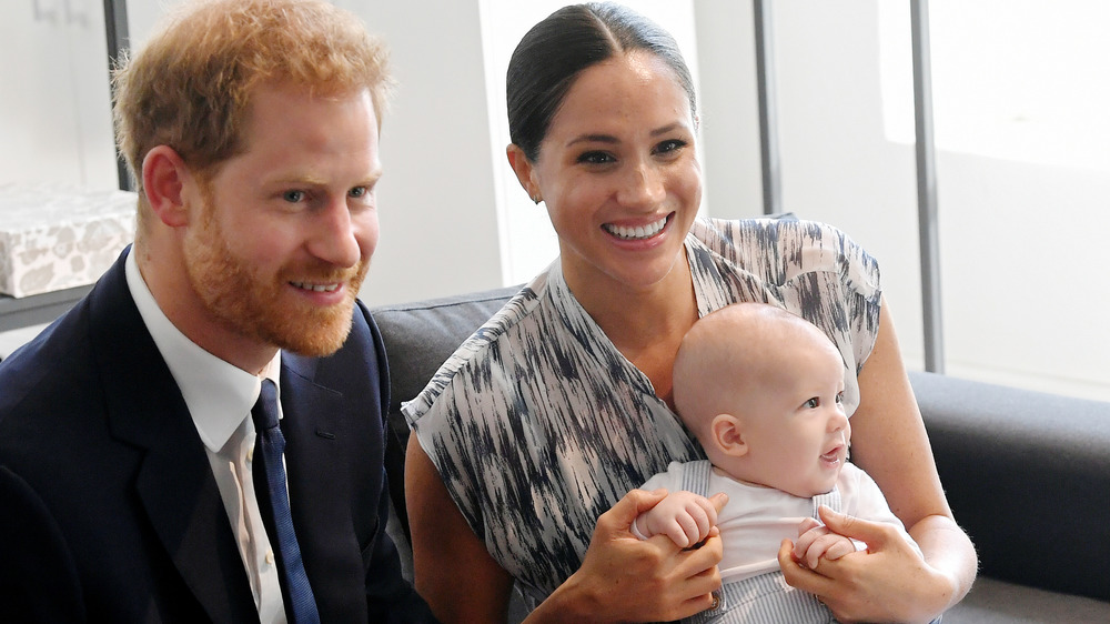Prince Harry seated next to Meghan Markle holding baby Archie
