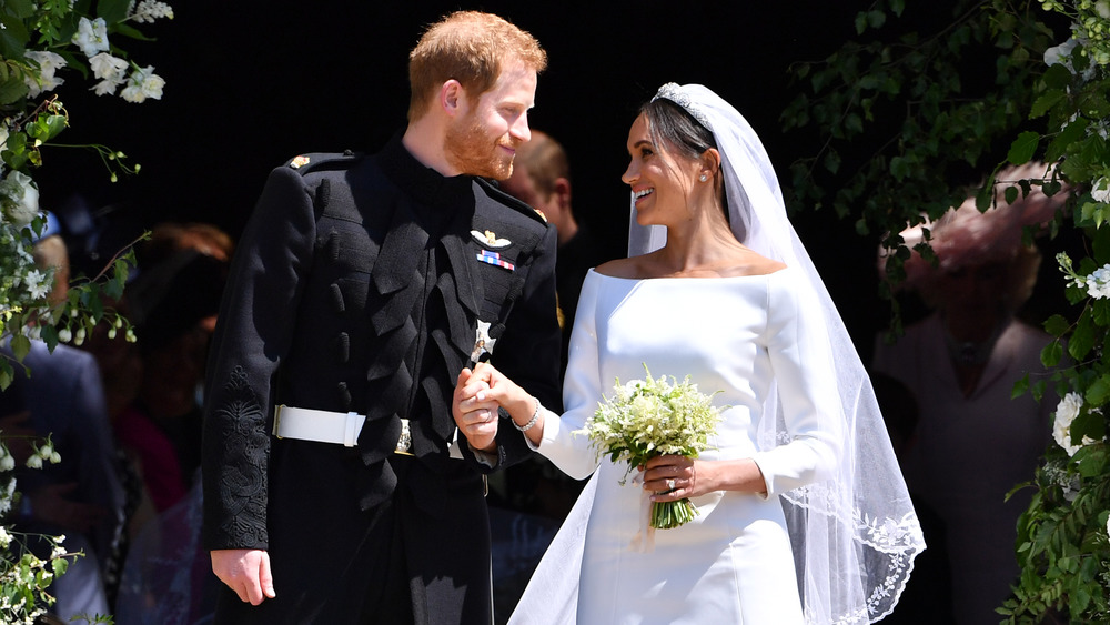 Prince Harry and Meghan Markle smiling and holdin ghands at their wedding 