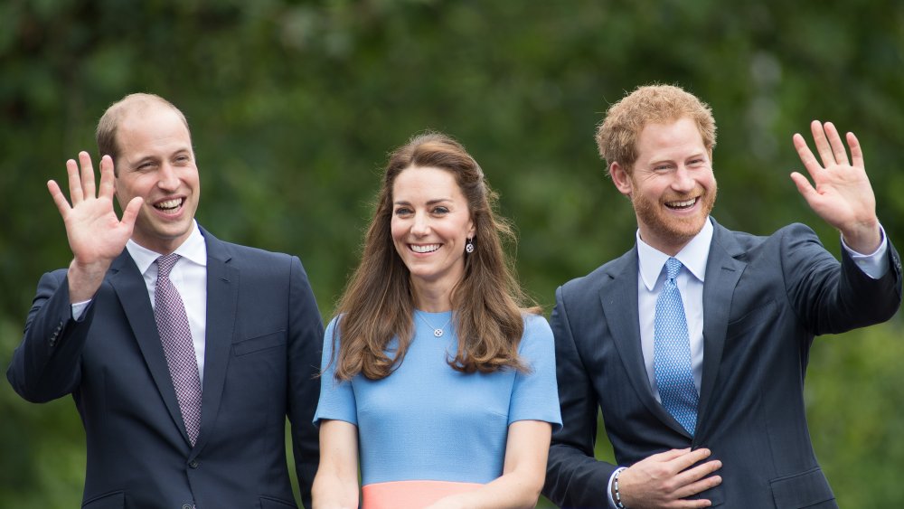 Prince William, Kate Middleton, Prince Harry smiling and waving, all dressed in blue