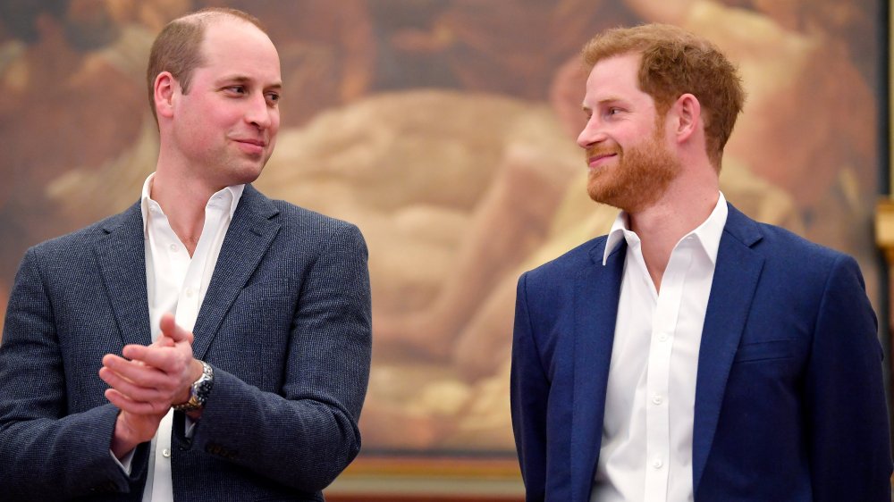 Prince William clapping and looking at Prince Harry, both smirking