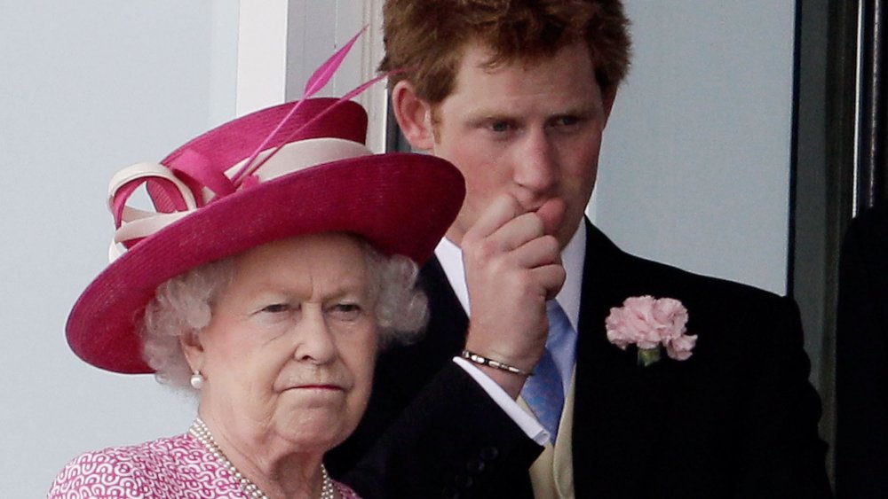 Queen Elizabeth in a pink hat-and-dress combo, looking serious in front of a young Prince Harry