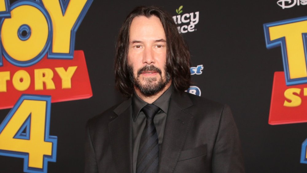 Keanu Reeves wearing a black suit with a blue-and-black striped tie, attending the Toy Story 4 premiere