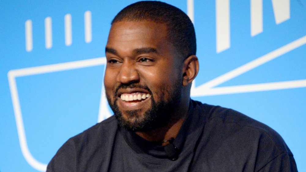 Kanye West in a dark blue shirt, smiling big during an interview