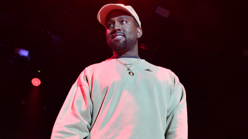 Kanye West in a white sweatshirt and baseball cap, looking out at the crowd during a concert