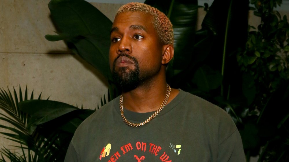 Kanye West in a grey, printed t-shirt and gold chain, looking off to the side with a serious expression