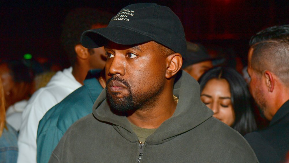 Kanye West in a grey hoodie and black hat, with a serious expression at an event