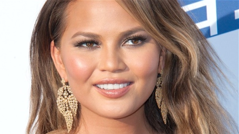 Chrissy Teigen smiling while wearing large earrings