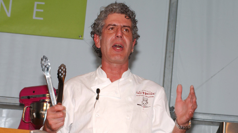 Anthony Bourdain holding tongs and speaking