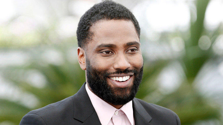John David Washington outdoors and smiling in a suit