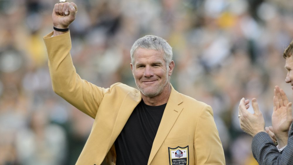 Brett Favre in a yellow Hall of Fame blazer, posing with his fist up in the air at a game